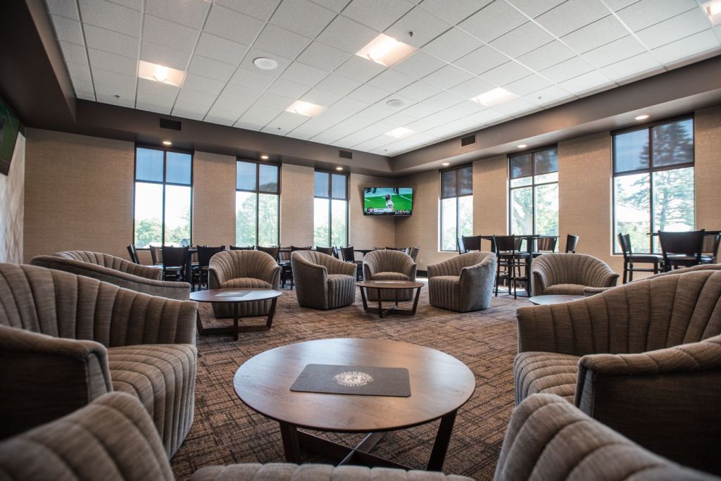 Photo of the members lounge, with comfortable lounge chairs, high tops, and TVs for watching sports.